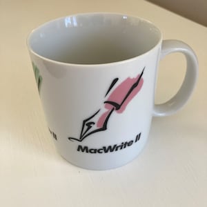 May include: White ceramic mug with a pink and black illustration of a pen and the text "MacWrite II" on the side.