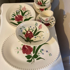 May include: A set of vintage floral dinnerware featuring a white background with a red, green, and blue floral pattern. The set includes a large oval platter, two dinner plates, a salad plate, a bowl, and two teacups.