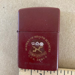 May include: A red lighter with a gold emblem that reads "Academy of Health Sciences", "To Conserve Fighting Strength", "U.S. Army", and "Ft. Sam Houston".