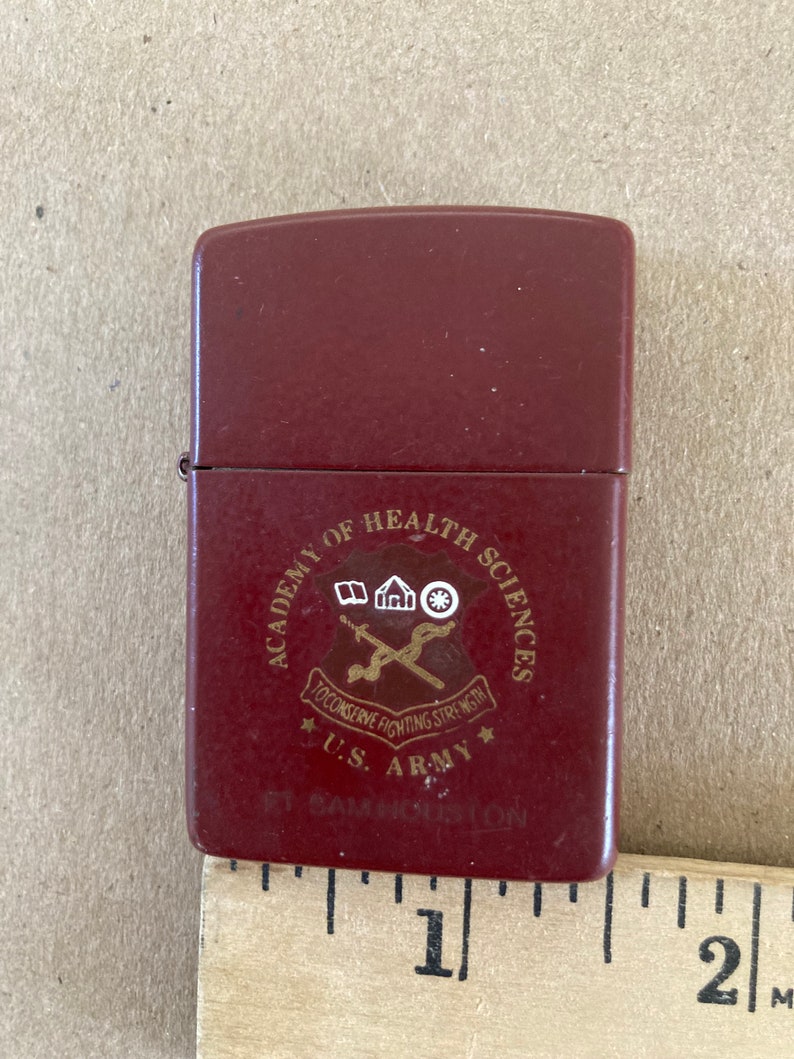 May include: A red lighter with a gold emblem that reads "Academy of Health Sciences", "To Conserve Fighting Strength", "U.S. Army", and "Ft. Sam Houston".