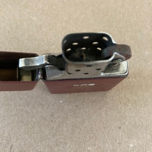 May include: A red lighter with a silver top and a black flint wheel. The lighter is open and the flint wheel is visible.