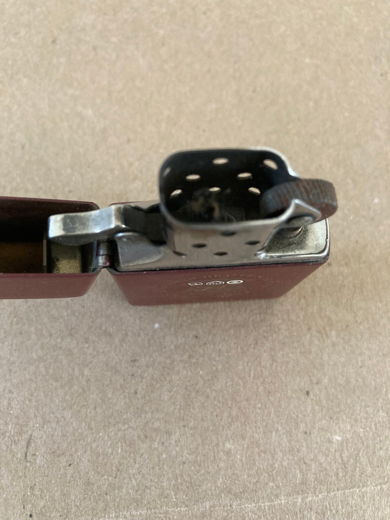 May include: A red lighter with a silver top and a black flint wheel. The lighter is open and the flint wheel is visible.