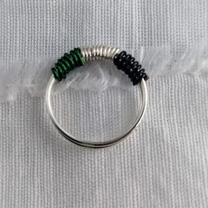 May include: A silver ring with green and black wire wrapped around it.