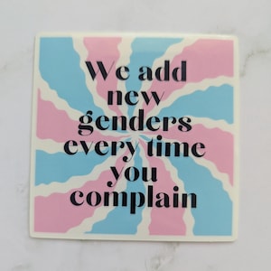 May include: A square sticker featuring a background of alternating wavy light blue and light pink rays radiating from the center. The text "We add new genders every time you complain" is printed in bold black serif font across the center.