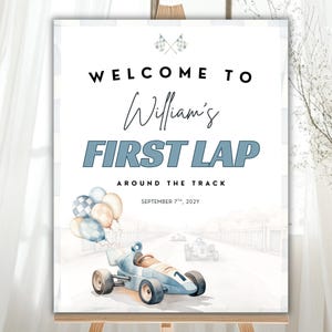 May include: A sign on an easel with the text "WELCOME TO William's FIRST LAP AROUND THE TRACK" in black and blue. The sign has a watercolor illustration of a race car and balloons. The date "SEPTEMBER 7th, 202Y" is also included.