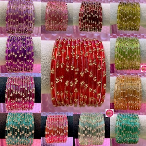 Op de afbeelding: Een verzameling kleurrijke armbanden in verschillende tinten, waaronder rood, paars, groen en roze. Elke armband is versierd met kleine, goudkleurige versieringen, wat een sprankelend effect creëert. De armbanden worden op een wit oppervlak gepresenteerd.