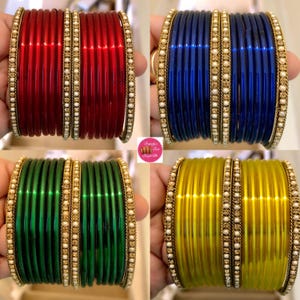 May include: Four sets of bangles in red, blue, green, and yellow. Each set is edged with a gold-coloured band and small white beads. The bangles have a glossy, solid colour.