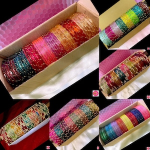 May include: A selection of colourful bangles in cardboard boxes. The bangles are arranged in rows, displaying a variety of colours including red, green, blue, yellow, and pink. Some bangles have small, decorative accents.