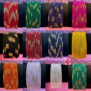 May include: A set of 12 colourful glass bangles with gold glitter accents. The bangles are arranged in rows of two, with each row featuring a different colour. The colours include red, green, blue, pink, black, yellow, orange, white, and purple.