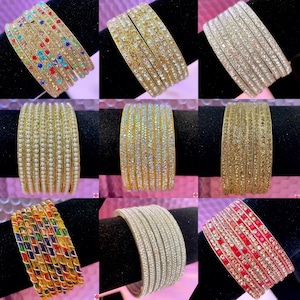 May include: Set of nine gold bangles with various embellishments, including colorful stones, pearls, and glitter.