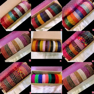 May include: A selection of vibrant bangles in shades of red, green, blue, and gold, presented in open cardboard boxes. The bangles are neatly arranged, highlighting their diverse designs and textures.