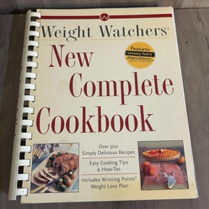 May include: A spiral-bound cookbook titled "Weight Watchers New Complete Cookbook." The cover is cream-colored with red text and features a gold seal that says "Features Winning Points Weight Watchers Weight Loss Plan."