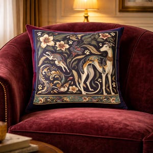 May include: A square throw pillow featuring a dark navy blue background with a detailed illustration of a greyhound standing and another running. The design includes cream-colored flowers, golden scrollwork, and small paw prints throughout.