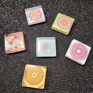 May include: Six square decorative tiles with colorful mandala designs. The tiles feature various color schemes, including orange, pink, yellow, green, and blue, with intricate patterns. The tiles are arranged on a dark, textured surface.