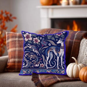 May include: A square throw pillow featuring a dark blue background with a repeating pattern of greyhound dogs, white flowers, swirling acanthus leaves, and small paw prints. The design includes a horizontal border at the bottom with floral motifs.