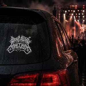 May include: A white vinyl decal featuring the stylized text Bring Me The Horizon in a jagged, metal-inspired font, applied to the rear window of a dark-colored vehicle covered in raindrops, with a blurred concert stage visible in the background.