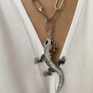 May include: A silver chain necklace with a large, silver lizard pendant. The lizard is covered in black and clear rhinestones.