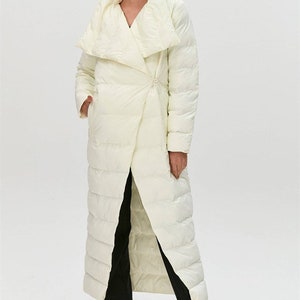 Peut inclure: Un long manteau blanc matelassé avec un grand col rabattu. Le manteau a une fermeture enroulée et un design matelassé.