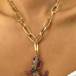 May include: A gold chain necklace with a large, jeweled lizard pendant. The lizard is pink, green, and gold with black eyes.