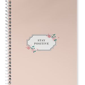 May include: A pink spiral bound notebook with a floral design and the text "STAY POSITIVE" in a gray frame.