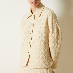May include: A cream-colored quilted jacket and matching skirt. The jacket has a button-up front and a patch pocket on the chest. The skirt has a scalloped hem and metal eyelets.