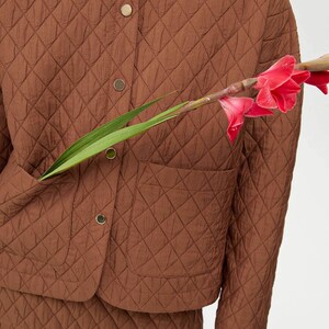 May include: A brown quilted jacket with a button-up front and a patch pocket on the left side. The jacket is made of a soft, lightweight fabric and has a relaxed fit.