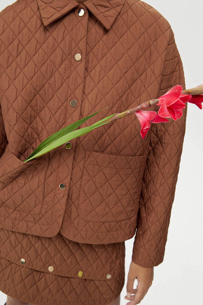 May include: A brown quilted jacket with a button-up front and a patch pocket on the left side. The jacket is made of a soft, lightweight fabric and has a relaxed fit.