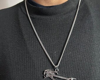 May include: A silver-toned metal necklace featuring a pendant shaped like an electric guitar. The guitar body has a stylized skull design, and the headstock is shaped like a hand making a rock-and-roll gesture. The pendant hangs from a thin chain.