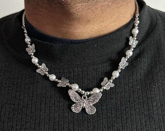 May include: A silver-toned necklace featuring a central butterfly pendant and smaller butterfly charms interspersed with round white beads. The chain is constructed with metallic links and beads, creating a symmetrical design around the neck.