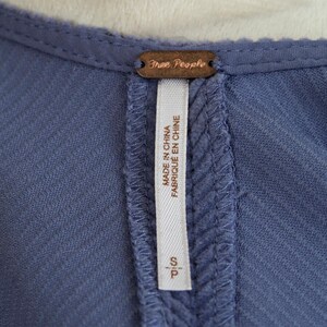 May include: Close-up of a blue garment with a textured fabric. A brown tag with the words "Free People" is at the top. A white tag with the text "MADE IN CHINA FABRIQU&Eacute; EN CHINE" and the size "S/P" is sewn into the garment.