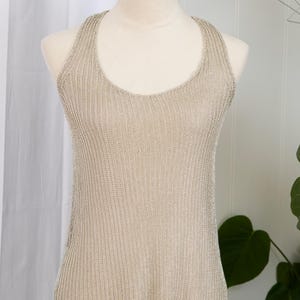 May include: A neutral-toned, sleeveless tank top with a scoop neck is displayed on a mannequin. The knit fabric has a subtle sheen. The top is a versatile piece of apparel.