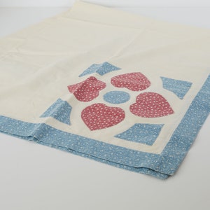May include: A white tablecloth with a blue and pink floral design. The tablecloth has a blue border with white polka dots.