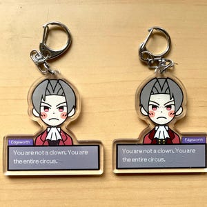 May include: Two clear acrylic keychains featuring a cartoon character with the text "Edgeworth You are not a clown. You are the entire circus."