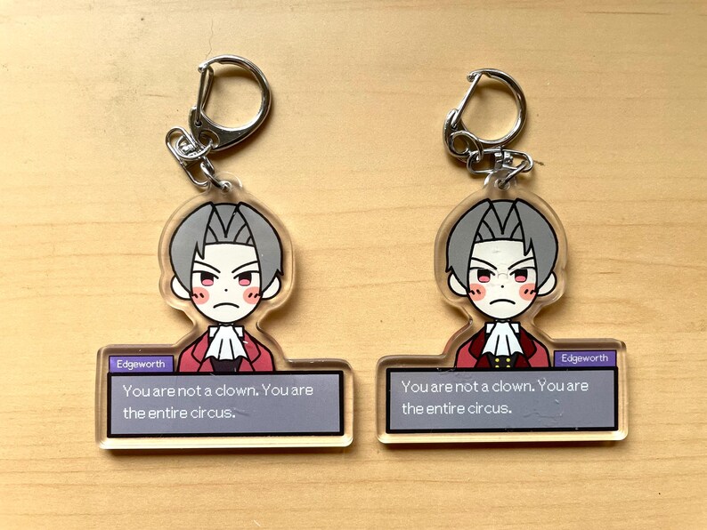 May include: Two clear acrylic keychains featuring a cartoon character with the text "Edgeworth You are not a clown. You are the entire circus."