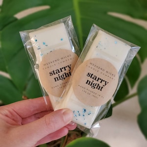 May include: Two white wax melts in clear plastic packaging. Each melt has blue glitter and a brown label that reads "Weekend Wicks Candle Company" and "Starry Night" with the text "Hand Poured" and "1.75 oz (50g)".