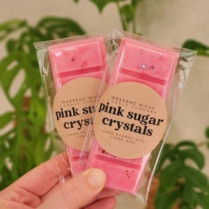 以下が含まれることがあります： 透明なパッケージに入ったピンクのワックスメルト2個。白いラベルには「Weekend Wicks Candle Company」と「Pink Sugar Crystals」の文字が書かれています。ワックスメルトはフロリダ州で手作りされており、1.75オンス（50g）です。