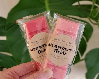 May include: Two pink wax melts in clear plastic packaging. The wax melts are labeled "strawberry fields" and are hand poured in 1.75 oz (50g).