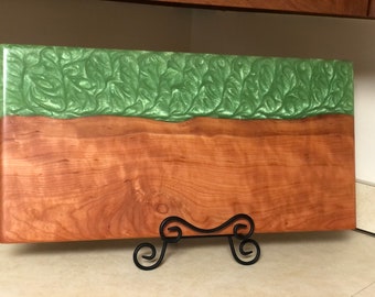 May include: A rectangular wooden cutting board with a green epoxy resin top. The board is on a black metal stand.