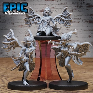 May include: Three gray, detailed, miniature figurines of winged creatures with sharp teeth and claws. The creatures are posed in different positions, with one kneeling, one standing with wings spread, and one standing with wings folded. The figurines are on a black base.