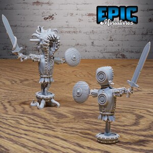 May include: Two gray painted miniature figures of fantasy creatures. One figure is a humanoid with a large head and a shield. The other figure is a humanoid with a large head and a sword. Both figures are standing on a base.