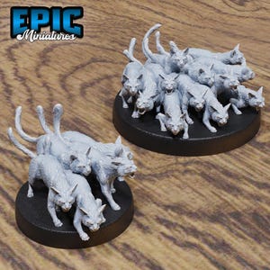 May include: Two miniature figurines of snarling cats in a light grey colour. Each figurine is mounted on a black circular base. The text "EPIC Miniatures" is in the upper left corner.