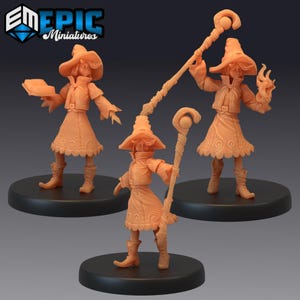 May include: Three orange miniature figurines of a witch with a hat, coat, and skirt. One holds a book, another a staff, and the third a staff and a flame. The figurines are on black circular bases.