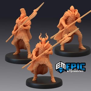 May include: Three miniature figurines of armored warriors in a light orange color, each holding a spear. The figures stand on black circular bases. One figure has a horned helmet, while the others have helmets with crests. The figures are in a battle-ready stance.