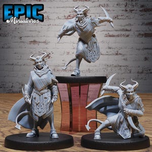 May include: Three gray miniature figures of horned, masked characters in dynamic poses. One figure is mid-jump, holding two curved blades. The other two figures are standing and kneeling, also holding blades. The figures have capes and detailed armor. The text "EPIC Miniatures" is in the upper left corner.