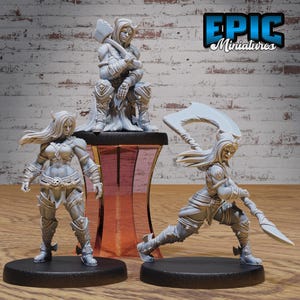 May include: Three unpainted miniature figures of female warriors, one sitting and two standing, holding weapons. The figures are made of a gray plastic material. The figures are on a black base and a brown base. The figures are from Epic Miniatures.