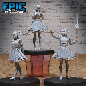 Peut inclure: Trois figurines miniatures peintes en gris d'un personnage féminin portant une tenue de femme de chambre avec un tablier à volants et un bandeau avec des cornes. Le personnage est posé de trois manières différentes, l'une tenant un petit objet, l'autre les bras tendus et la dernière les bras le long du corps. Les figurines sont posées sur des socles noirs.
