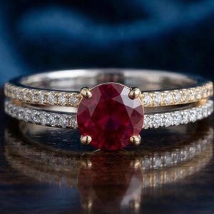 Puede incluir: Un juego de anillos de dos piezas con una gema roja oscura grande y redonda en un engaste de oro. La banda está adornada con pequeñas gemas claras. La segunda banda también tiene pequeñas gemas claras.