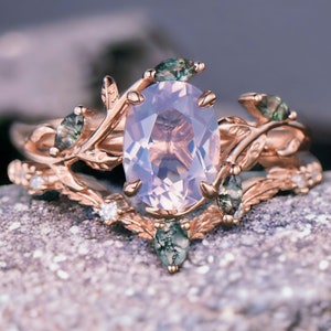 Könnte beinhalten: Ein Ring aus Roségold mit einem zarten, blattförmigen Design. Der Ring hat einen großen ovalen rosafarbenen Edelstein, der von kleineren grünen Edelsteinen umgeben ist.