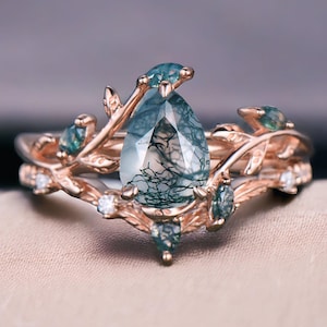 Peut inclure: Un ensemble de bagues en or rose avec une pierre d'agate mousse en forme de poire. La bague est ornée de détails de feuilles et de vignes, rehaussés de petites pierres précieuses rondes et transparentes. L'agate mousse présente un motif naturel unique d'inclusions vertes.