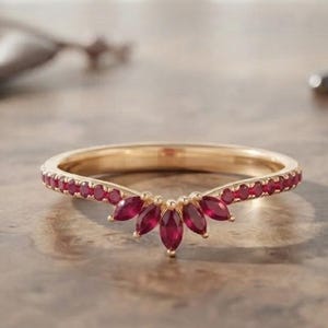 Puede incluir: Un anillo de oro con un diseño en forma de V, adornado con pequeñas piedras rojas redondas a lo largo de la banda y cinco piedras rojas de talla marquesa dispuestas en abanico en el punto central de la montura en V.